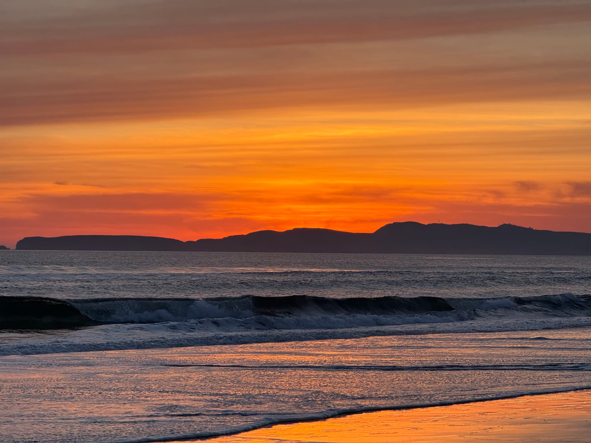Sunset waves rolling toward a beach under an orange and violet sky