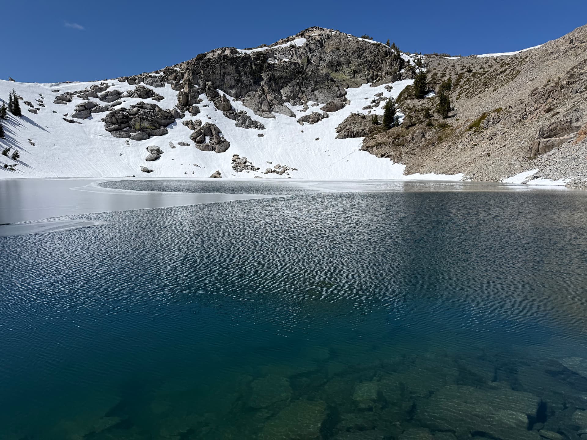 A partly frozen alpine lake tucked beneath a rocky, snow-dusted ridge