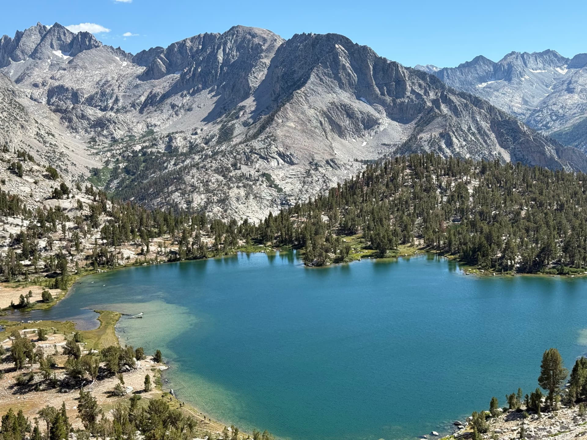 A turquoise alpine lake backed by a wall of gray Sierra peaks and pine forest