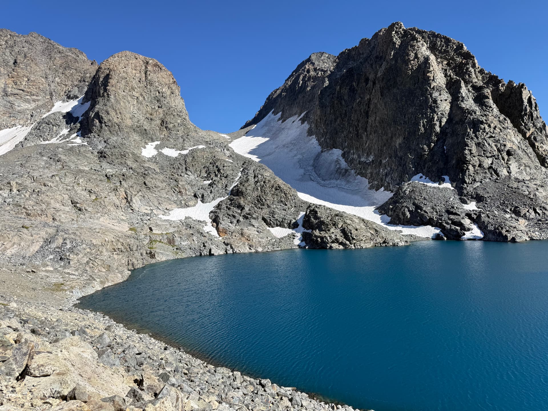 A deep cobalt alpine lake tucked beneath towering gray peaks and patches of snow