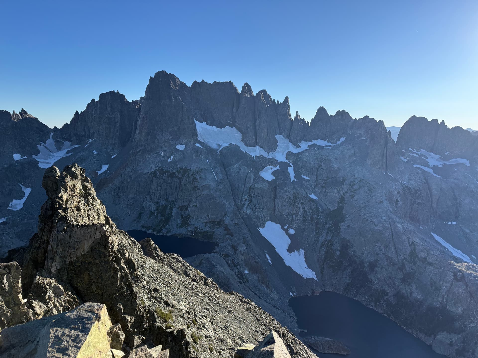 Jagged granite peaks and remnant snowfields above dark alpine lakes