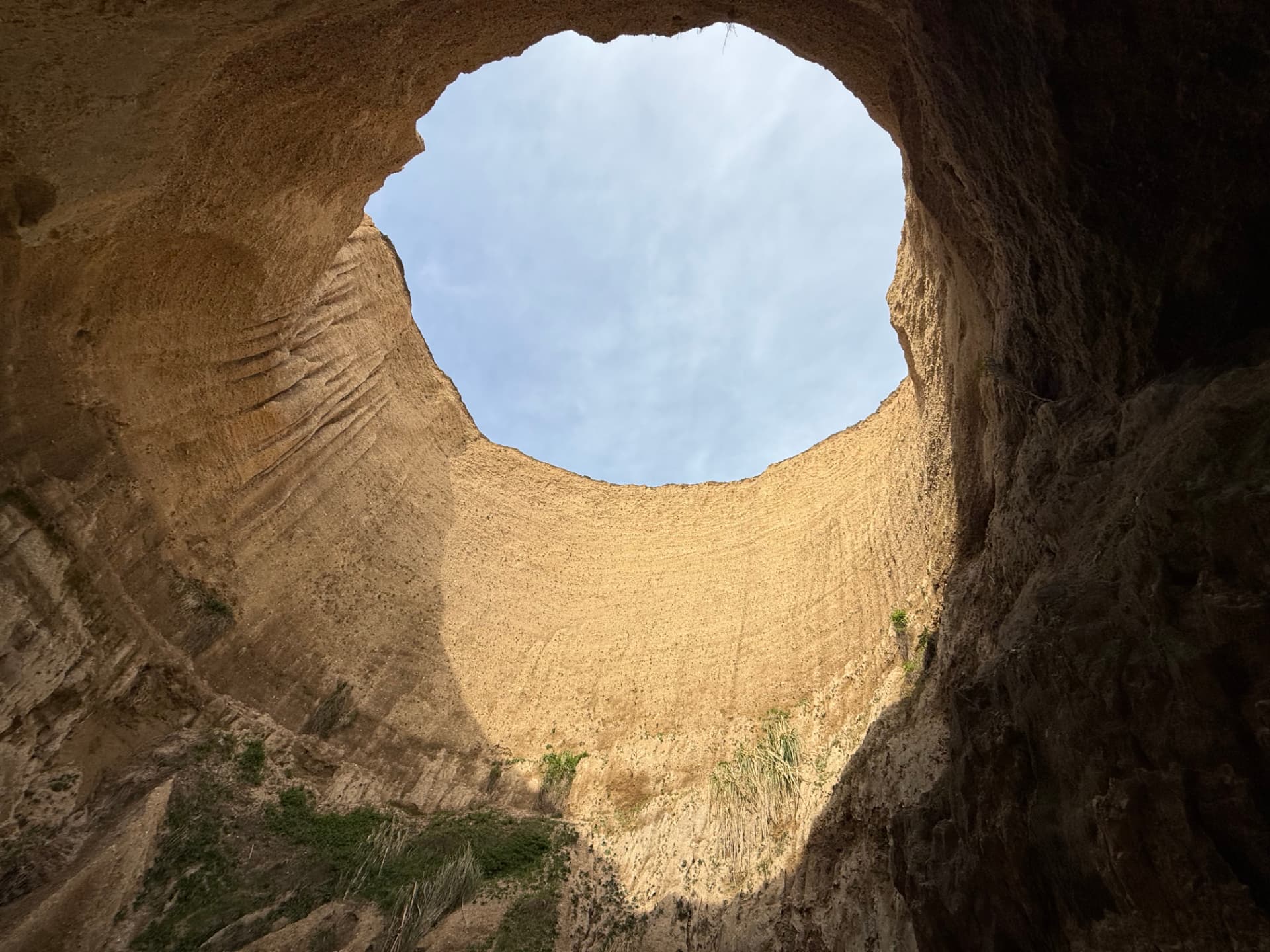 A view looking up through a sandstone arch toward a bright blue sky